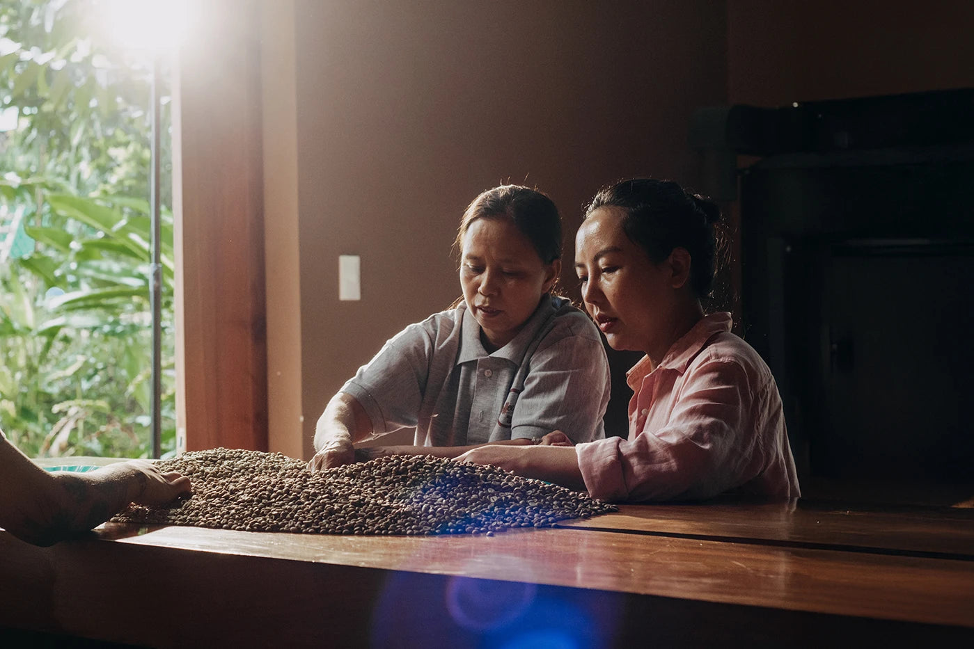 Timen and Scott examining coffee beans at a processing site, surrounded by blue barrels and machinery.